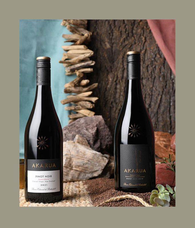 Two bottles of Akarua wine against a natural background with rocks and driftwood.